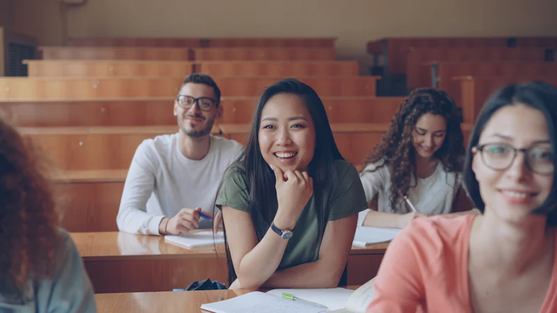 Grupo de estudiantes, en su mayoría mujeres, sonríe con sus apuntes en un aula universitaria